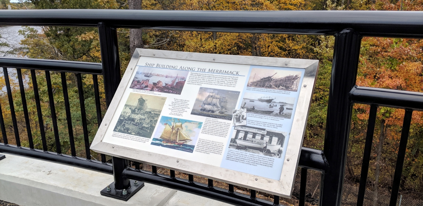 Interpretive Panel titled "Ship Building Along the Merrimack" installed on the Whittier Bridge at Garrison Trail with fall foliage in the background.
